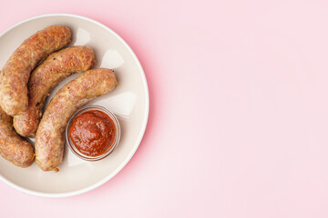 Plate of tasty homemade sausages with sauce on pink background