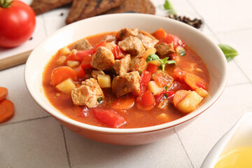 Bowl of tasty beef stew on white tile background