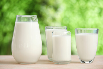Glasses and jug of fresh milk on beige table outdoors