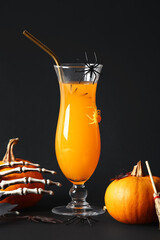 Glass of delicious orange cocktail, skeleton hand and pumpkins for Halloween celebration on black background