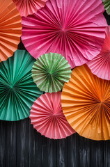 A large photo booth backdrop , featuring a gradient of pink, orange, and green paper fans against dark wood paneling, creating a vibrant and celebratory atmosphere.Copy space,flat lay.