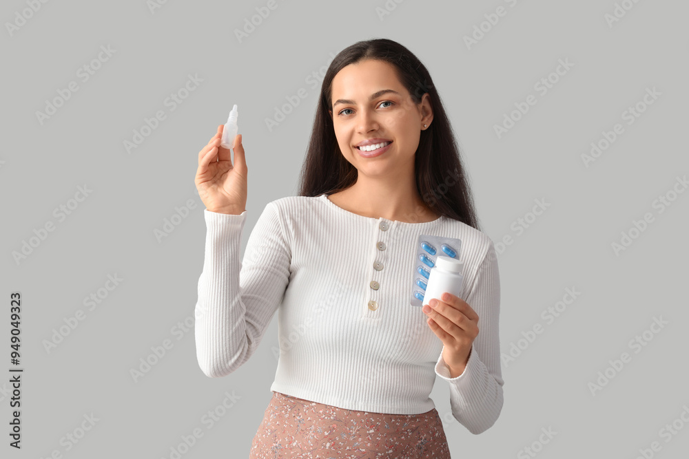 Wall mural young woman with nasal drops and pills on grey background