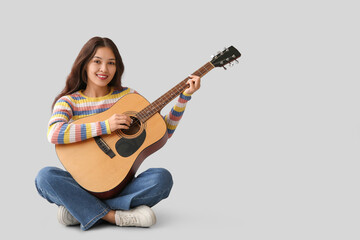 Young woman playing guitar on grey background