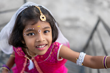 A young girl in vibrant traditional attire smiles warmly while climbing stairs during a festive...