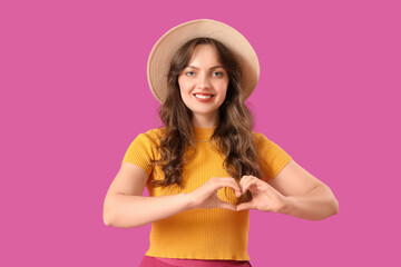 Beautiful young woman showing heart gesture on purple background. Valentine's Day celebration
