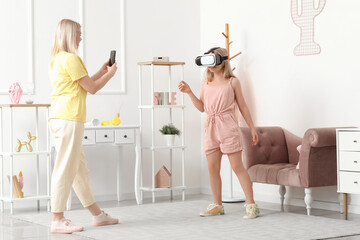 Beautiful female blogger recording on camera her daughter in VR glasses at home