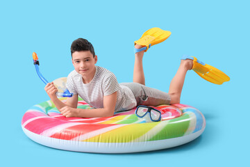 Cute little boy with inflatable mattress, snorkeling mask and flippers on blue background © Pixel-Shot
