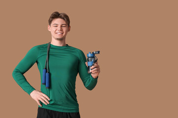 Sporty young man with bottle of water and jumping rope on brown background