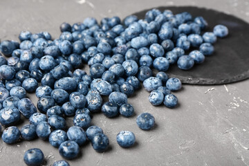 Black board with sweet fresh blueberries on grey background