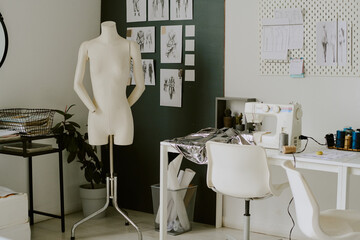 Creamy colored mannequin standing next to white table with metallic piece of fabric and white sewing machine