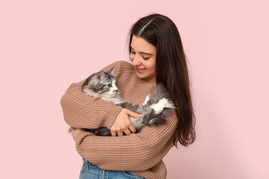 Young woman with cute longhaired cat on pink background