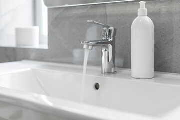 Liquid soap bottle on white washbasin at home in bathroom, pouring water, flowing from the tap