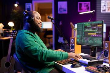 Sound technician playing piano notes to edit with DAW software in his home studio, working at night...