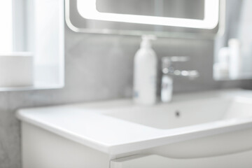 Closeup of white washbasin, chrome faucet and soap bottle blurred on background, bathroom with grey tile walls