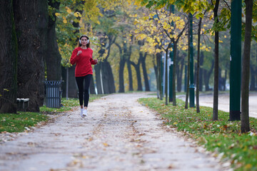 Young beautiful woman running in autumn park and listening to music with headphones on smartphone