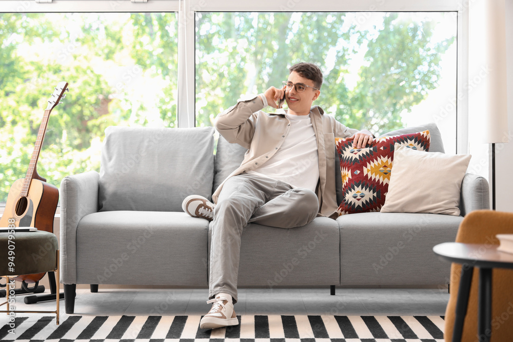 Poster Young man in eyeglasses talking by mobile phone on sofa at home