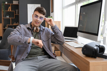 Young man checking smartwatch at desk in office