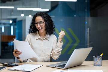 Happy businesswoman celebrating achievement in office while reviewing important documents. Woman...