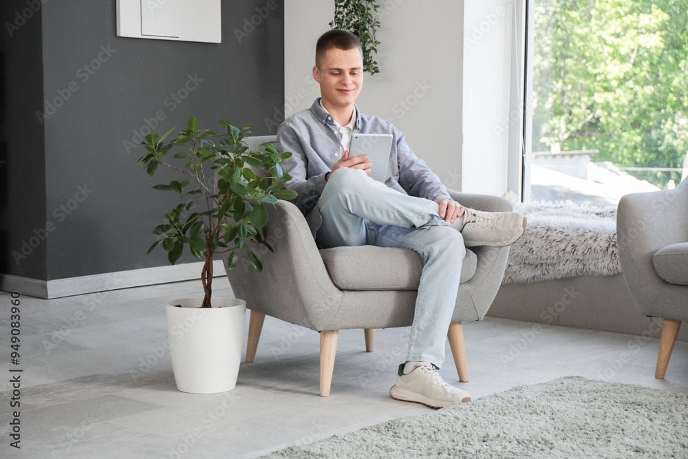 Wall mural young male freelancer with tablet computer sitting on armchair in modern home office