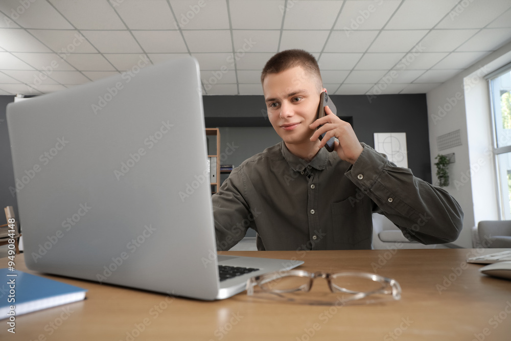 Poster Young male businessman with laptop talking by phone in modern home office