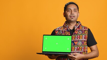 Upbeat tech specialist doing promotion using isolated screen laptop, studio background. Cheerful indian person holding chroma key notebook, doing advertisement for it, camera A