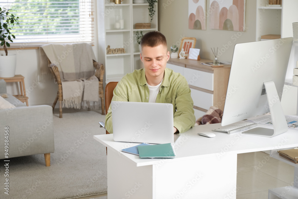 Poster young male freelancer working with laptop and computer in light home office