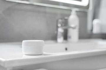 White cream jar with space for design on washbasin in bathroom. Natural cosmetic product in a container for facial care