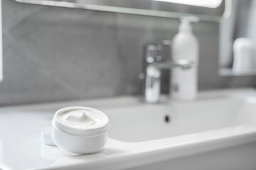 White opened cream jar on washbasin in bathroom, close up, mockup. Cosmetic mockup for brand packaging