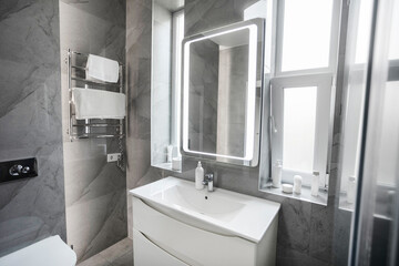 Mirror with led lighting above white washbasin on wall with grey tiles , modern minimalist bathroom...