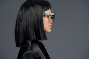 Fototapeta premium Woman with black hair, glasses, and black jacket, eyes closed, looking to the side against gray background
