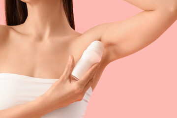 Beautiful young woman applying deodorant on pink background, closeup