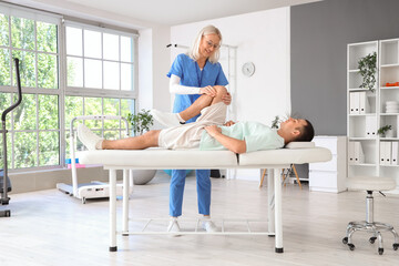 Female physiotherapist working with lying young man on couch in rehabilitation center