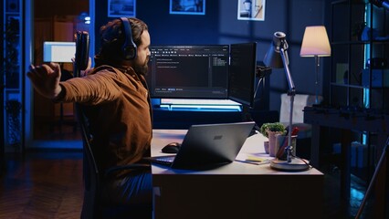 Software programmer taking break from coding, putting headphones on and stretching on desk chair...