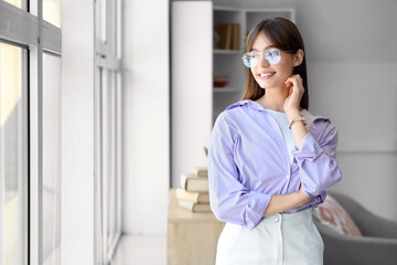 Young woman in eyeglasses near window at home