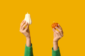 Fototapeta premium Female hands with autumn candles in shape of pumpkins on yellow background