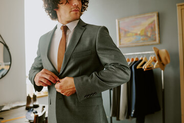 Unrecognizable man buttoning gray jacket while looking in mirror