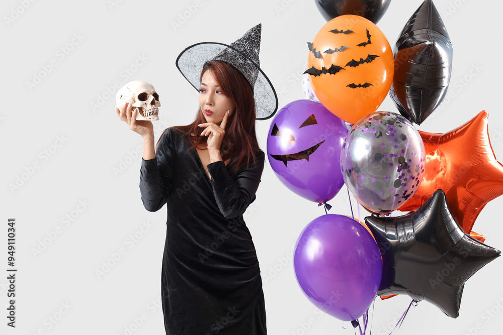 Sticker thoughtful young asian woman dressed for halloween as witch with skull and balloons on light backgro