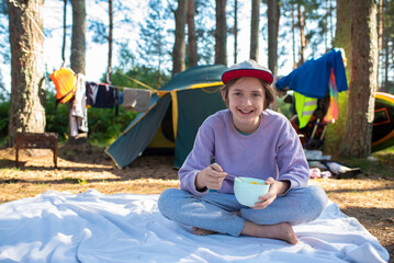 An 11 year old boy or teenager has breakfast with cereal and milk, sitting on a blanket in front of...