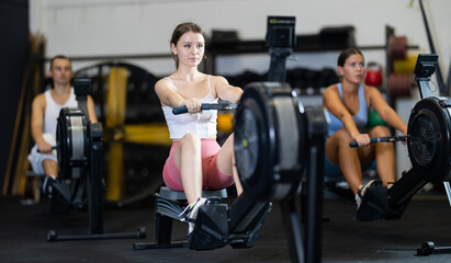 Young woman in sportswear training on rowing machine in gym