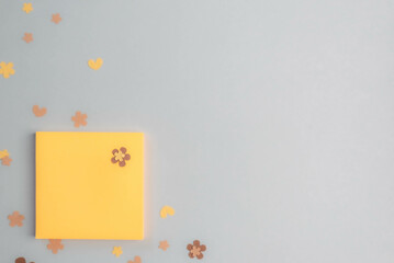 Blank, square, yellow paper notepad on dreamy gray background with flower cutouts.