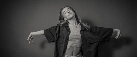 A woman is posing gracefully with her arms extended, wearing a loose shirt and crop top, against a minimalistic background, creating a sense of freedom and artistic expression.