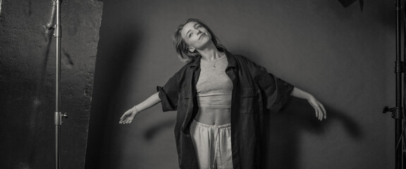 Obraz premium A black and white image of a woman posing with her arms outstretched in a studio, wearing casual clothes, conveying a sense of freedom and expression through body language.