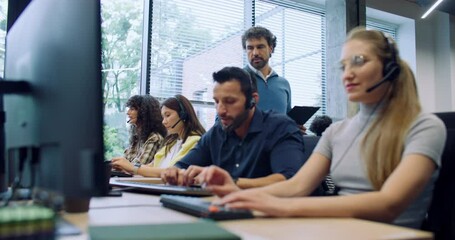 Hardworking dispatchers or consultants actively talking with clients on headsets. Attractive leader walking in background and controlling work process. People using computers at work. Support center. - Powered by Adobe