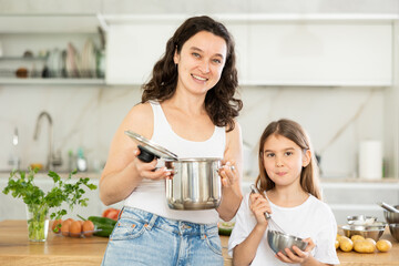 Woman and her daughter pose in kitchen with dishes in their hands. Mom and daughter have nice time...