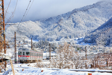 雪が積もった焼額山を背景に長野電鉄が大カーブを進む