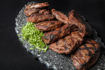 Grilled steaks on a stone serving plate and black background