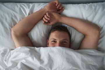 Relax, man and blanket portrait in bed with wake up, resting and sleeping in morning for holiday. Person, above and smile with duvet in bedroom for break, comfortable and peaceful in home on vacation