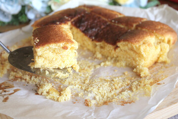 Fresh Baked Homemade Yellow Honey Cornbread Sliced on Parchment Paper with a Serving on a Plate and Milk