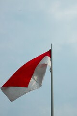 The Indonesian flag is red and white with an iron pole against a cloudy sky background.