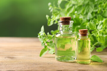 Essential oil in bottles and oregano twigs on wooden table against blurred green background, closeup. Space for text